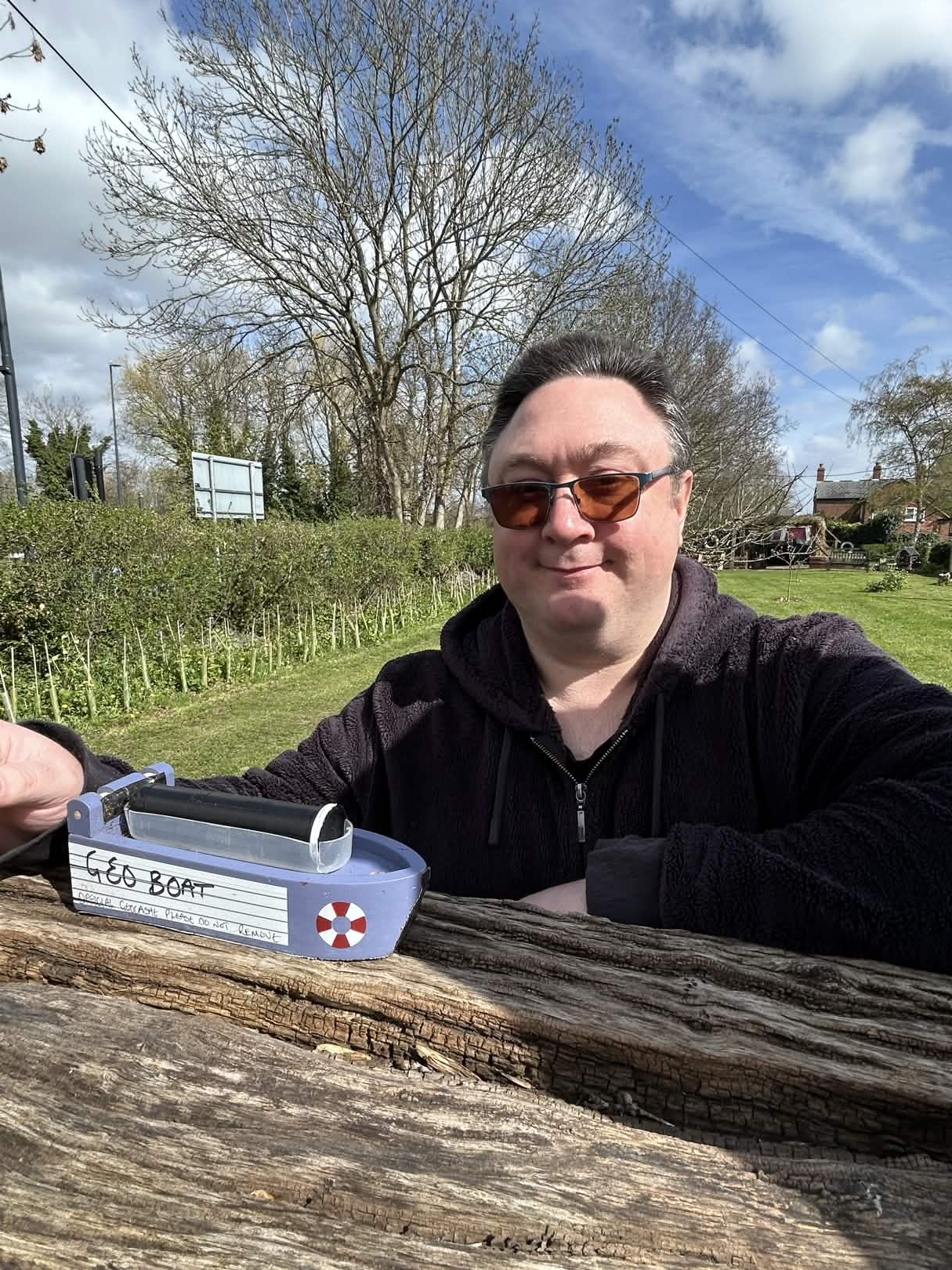 Ralph wearing sunglasses and posing with a geocache